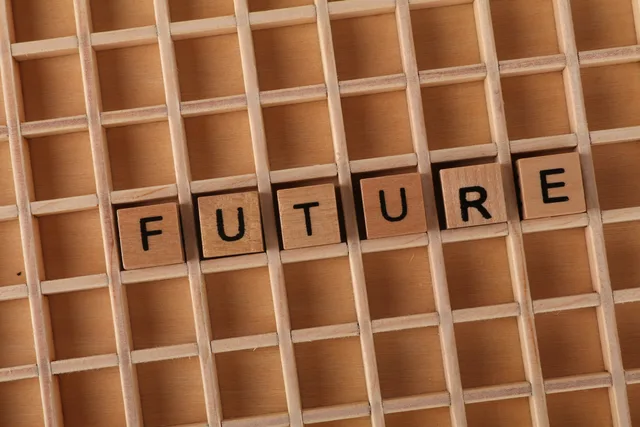 Wooden letter blocks spell 'FUTURE' on a wooden grid background. Media forecasting and scenario planning